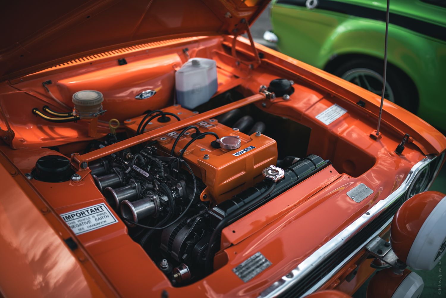 Close-up of an orange car engine compartment, featuring a well-maintained engine with various components and labels visible.