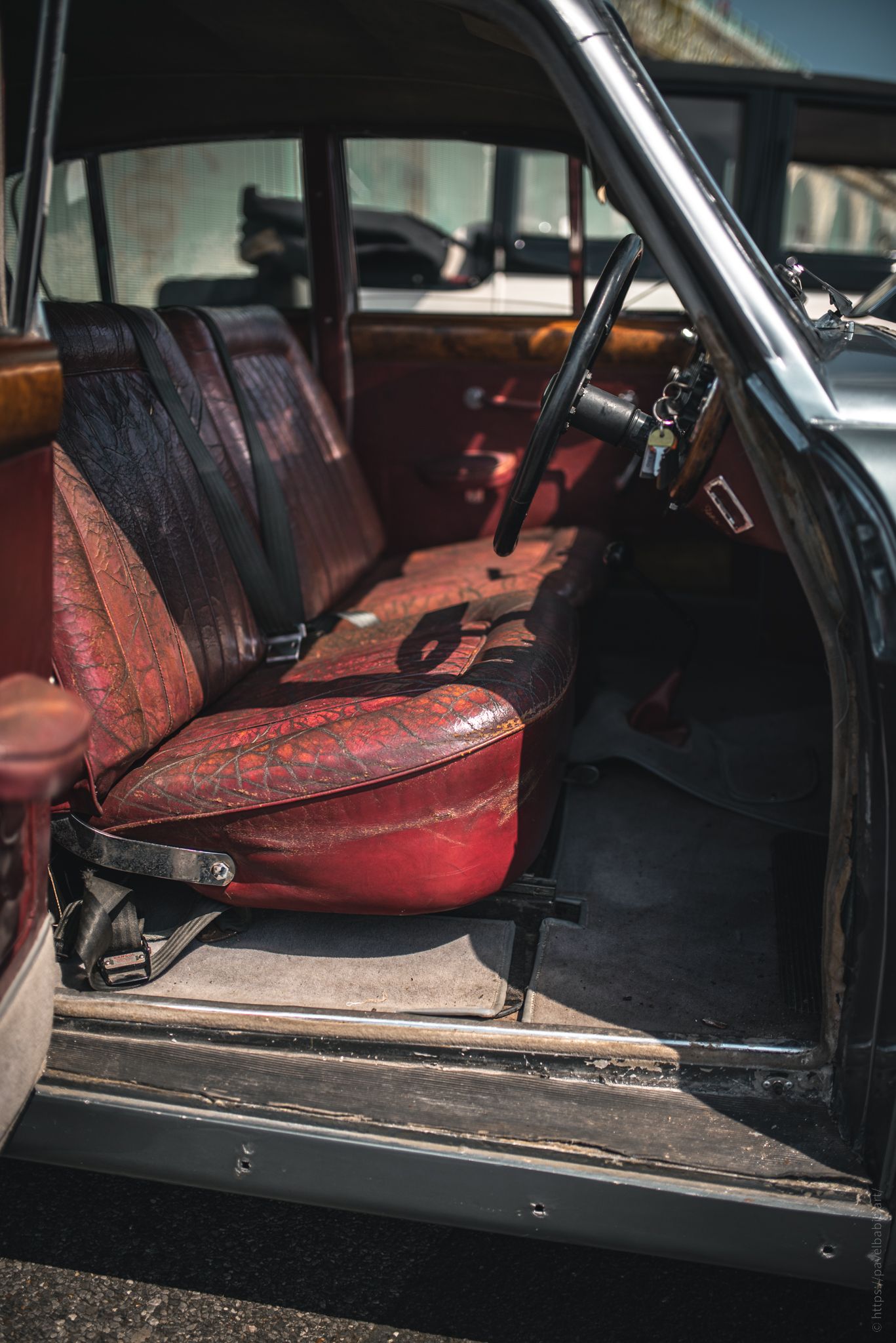 Vintage car interior showcasing worn red leather seats and a classic steering wheel, reflecting its age and character.