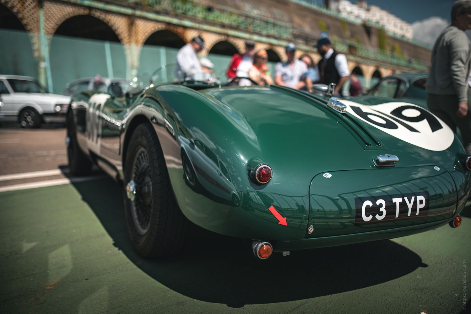A classic green sports car with the number 69 parked, surrounded by spectators at a lively event.