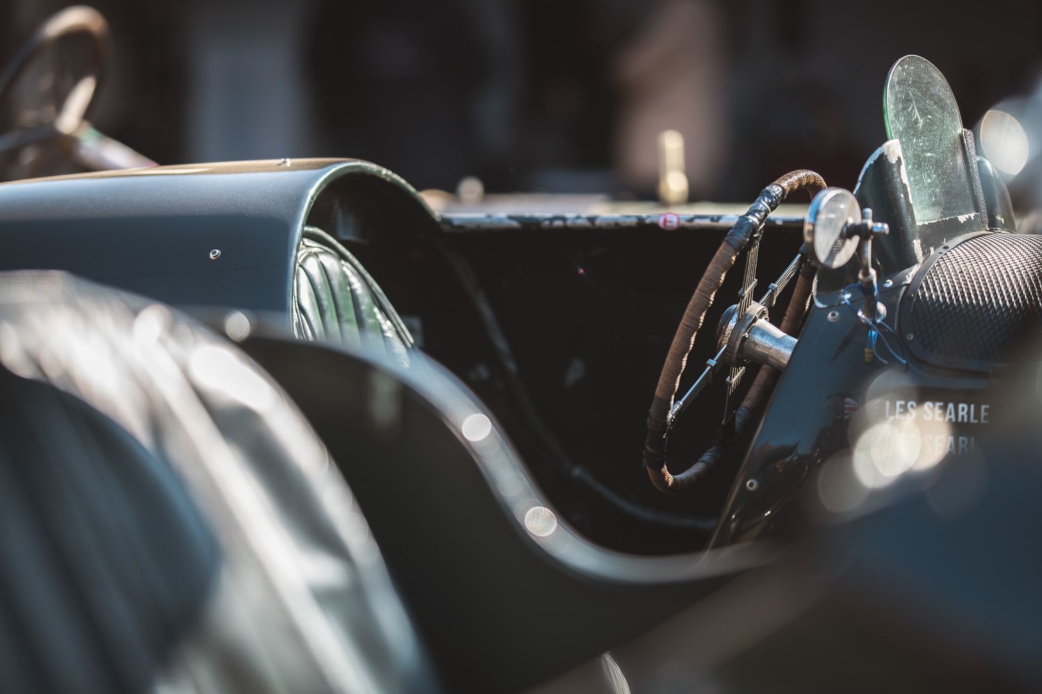 Close-up of a vintage sports car interior featuring a wooden steering wheel and elegant leather seats, exuding classic elegance.