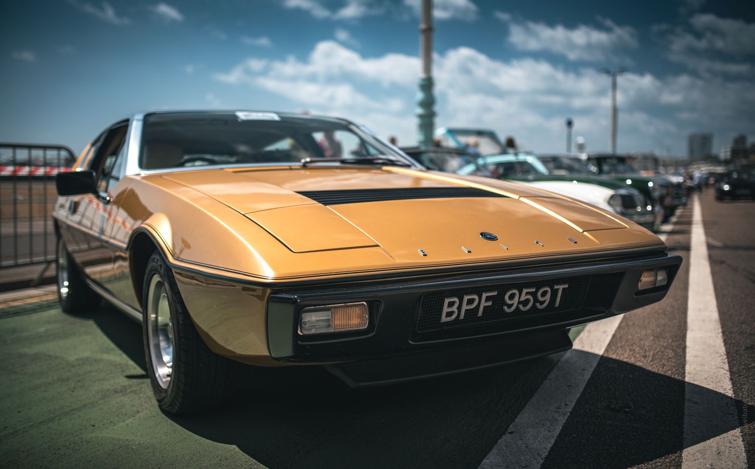 A vintage yellow car parked on a sunny day, showcasing sleek lines and detailed design against a blue sky.