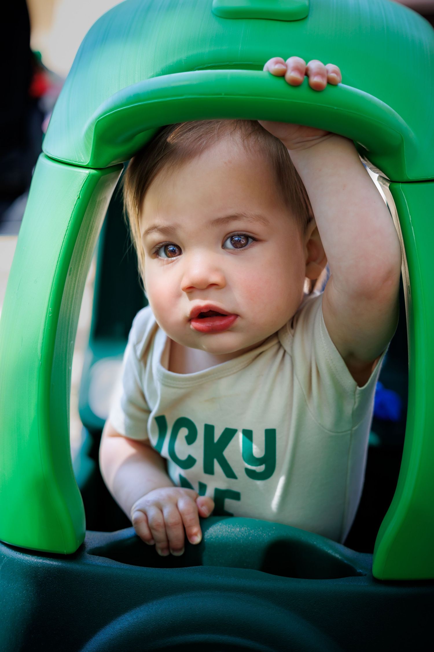 Young child in green toy car wearing light colored shirt.