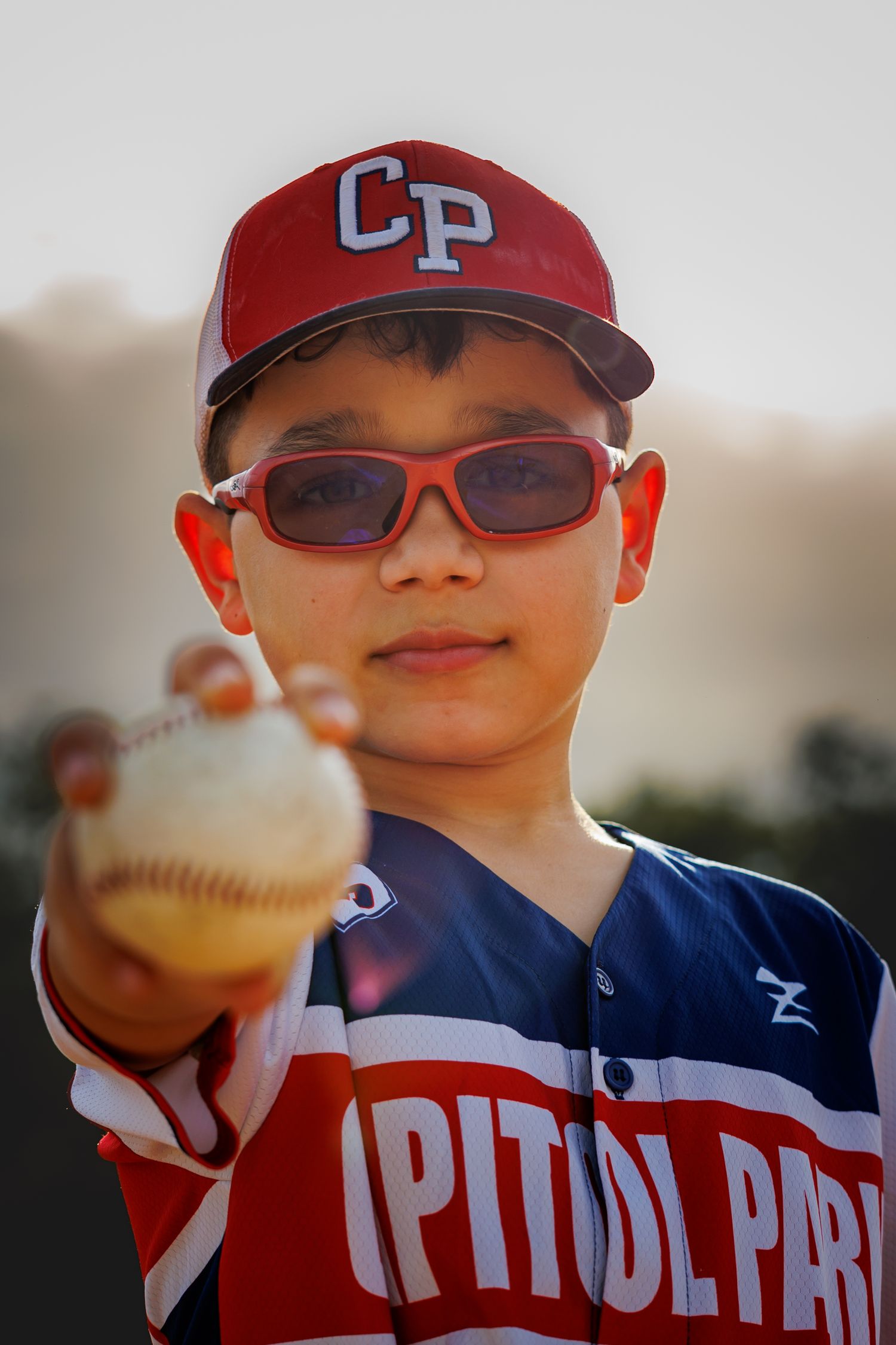 Baseball player in CP cap and sunglasses holding baseball while wearing team uniform.