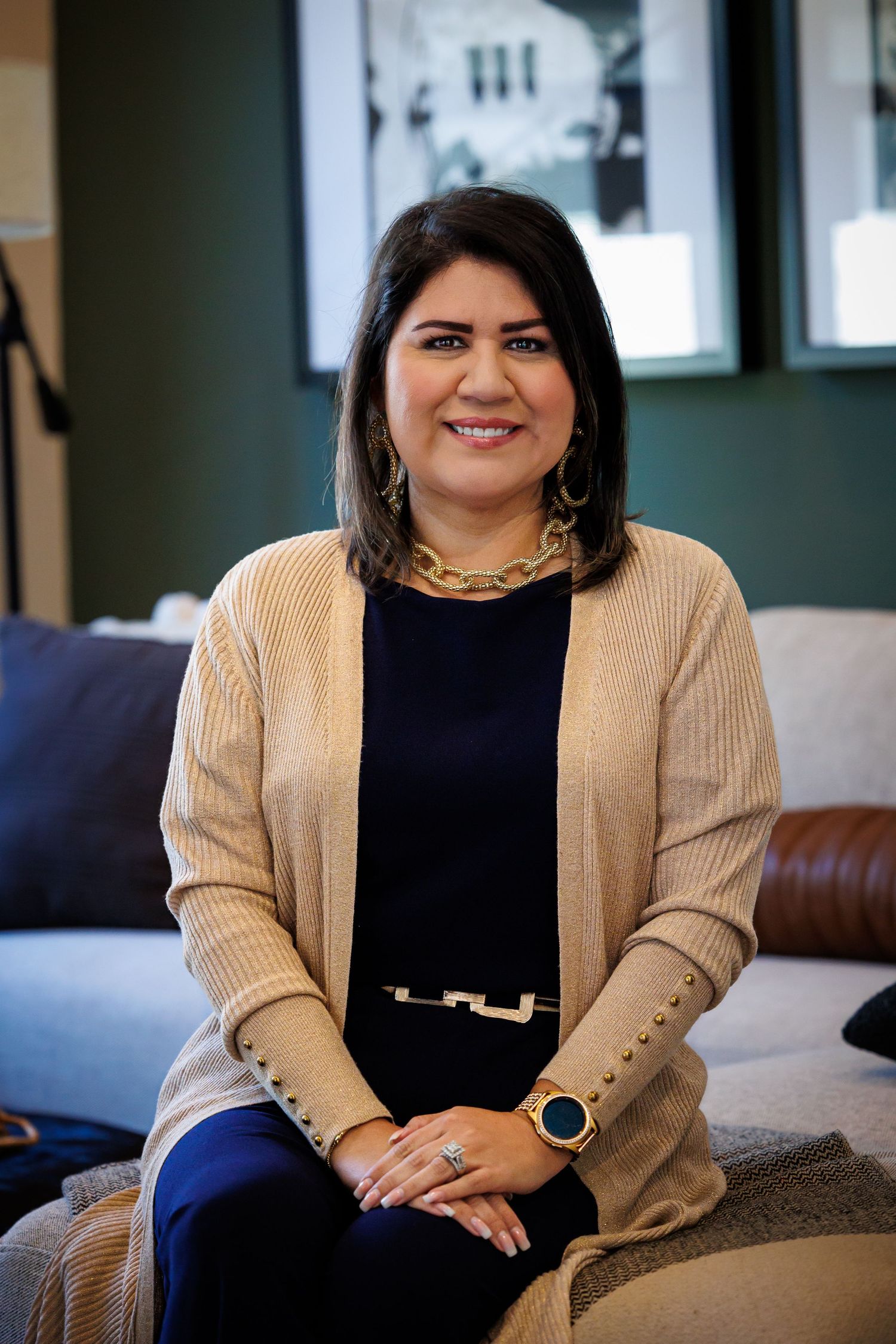 Professional portrait of someone wearing a beige cardigan and black top sitting on a brown leather couch in an office setting.