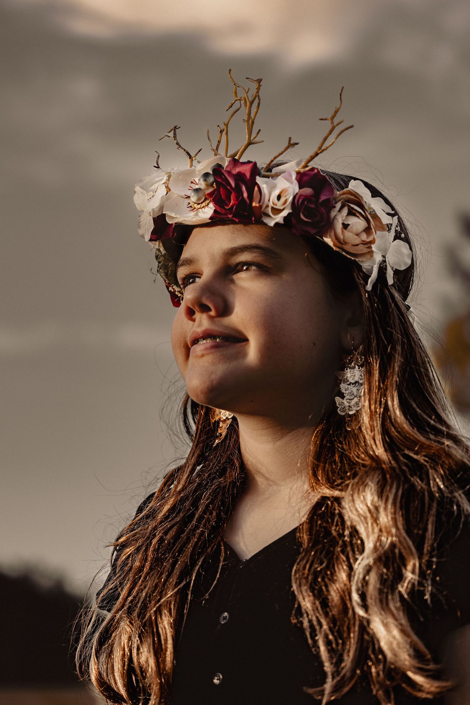 Person wearing floral crown looking up at sunset with warm lighting.