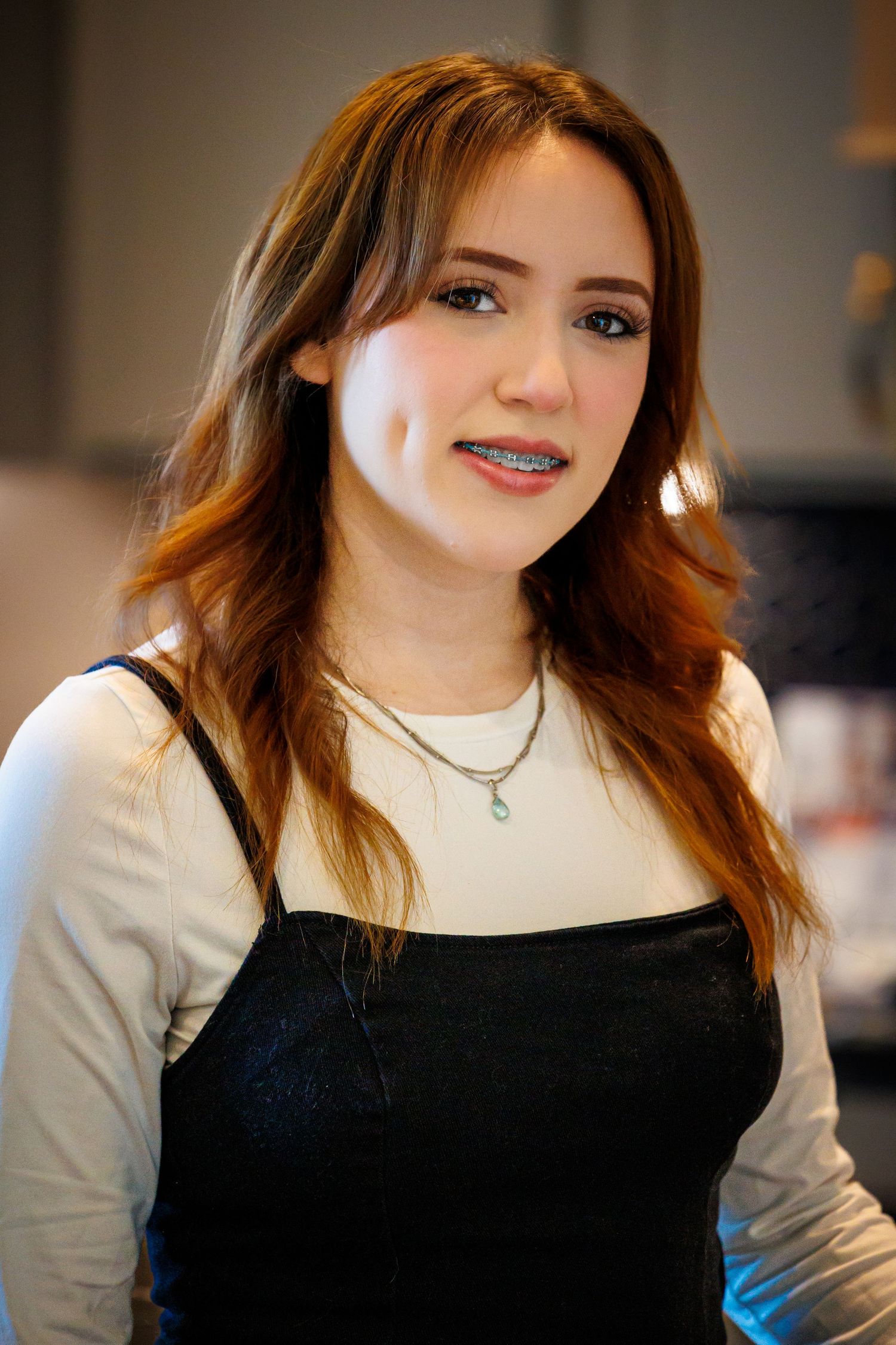 A person wearing a black top and white long sleeve shirt smiles warmly in an indoor setting.