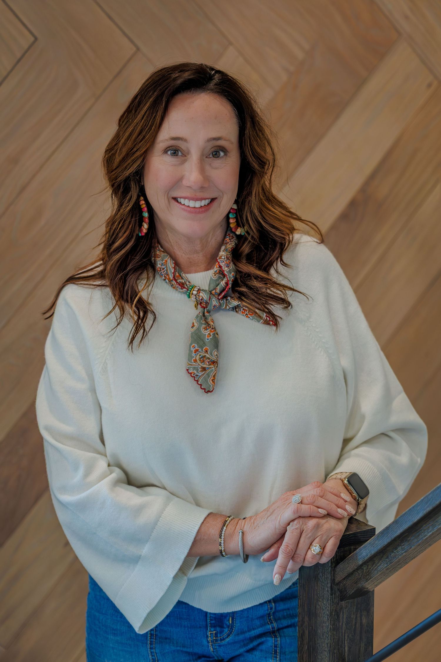 Professional headshot series showing person in white sweater and floral scarf against wooden wall background.