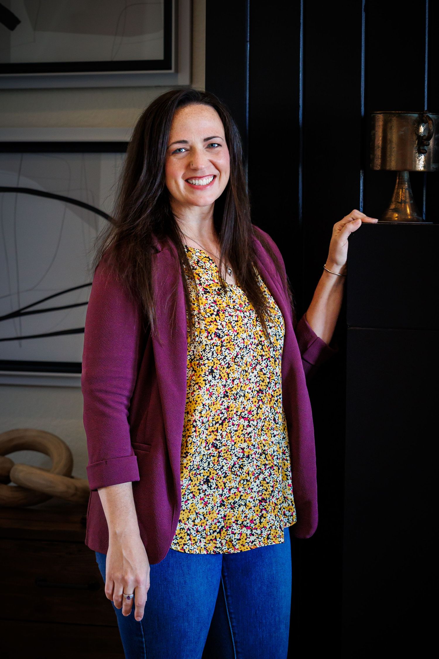 A person in a purple cardigan and floral top poses against a dark background.