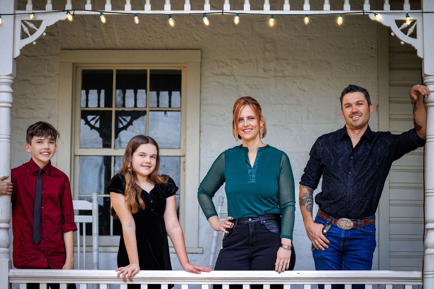 Family of four posing on white porch with decorative trim.