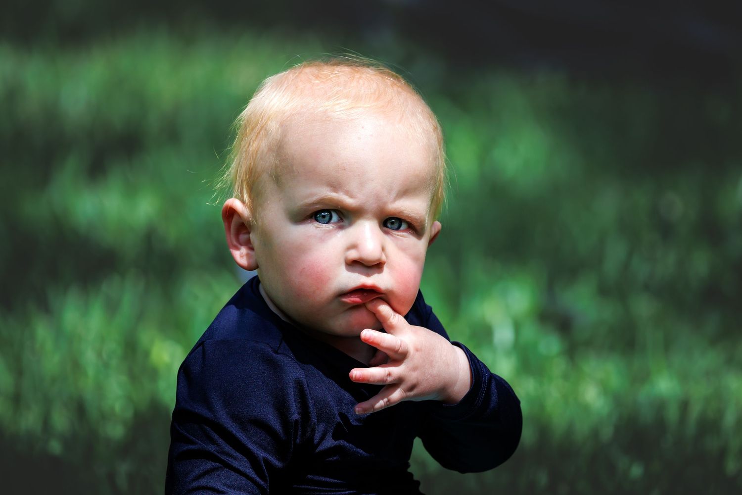 Young toddler with thoughtful expression against blurred green background.