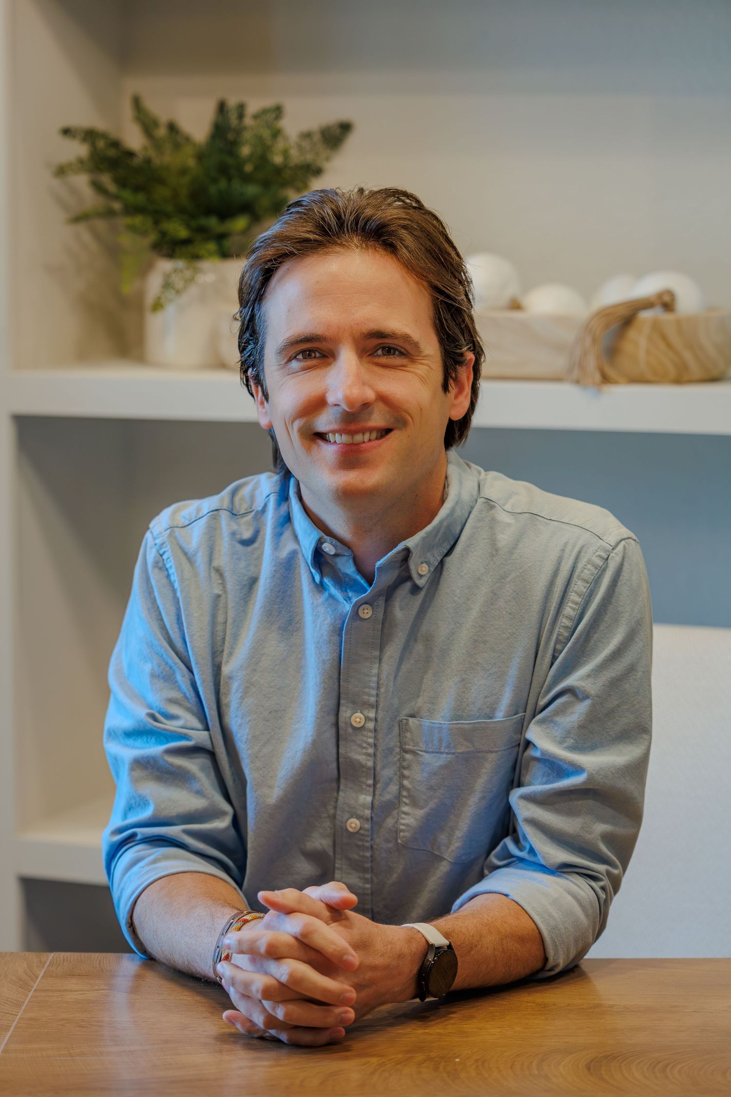 Professional headshot series showing person in blue button-down shirt sitting at wooden table in office setting.