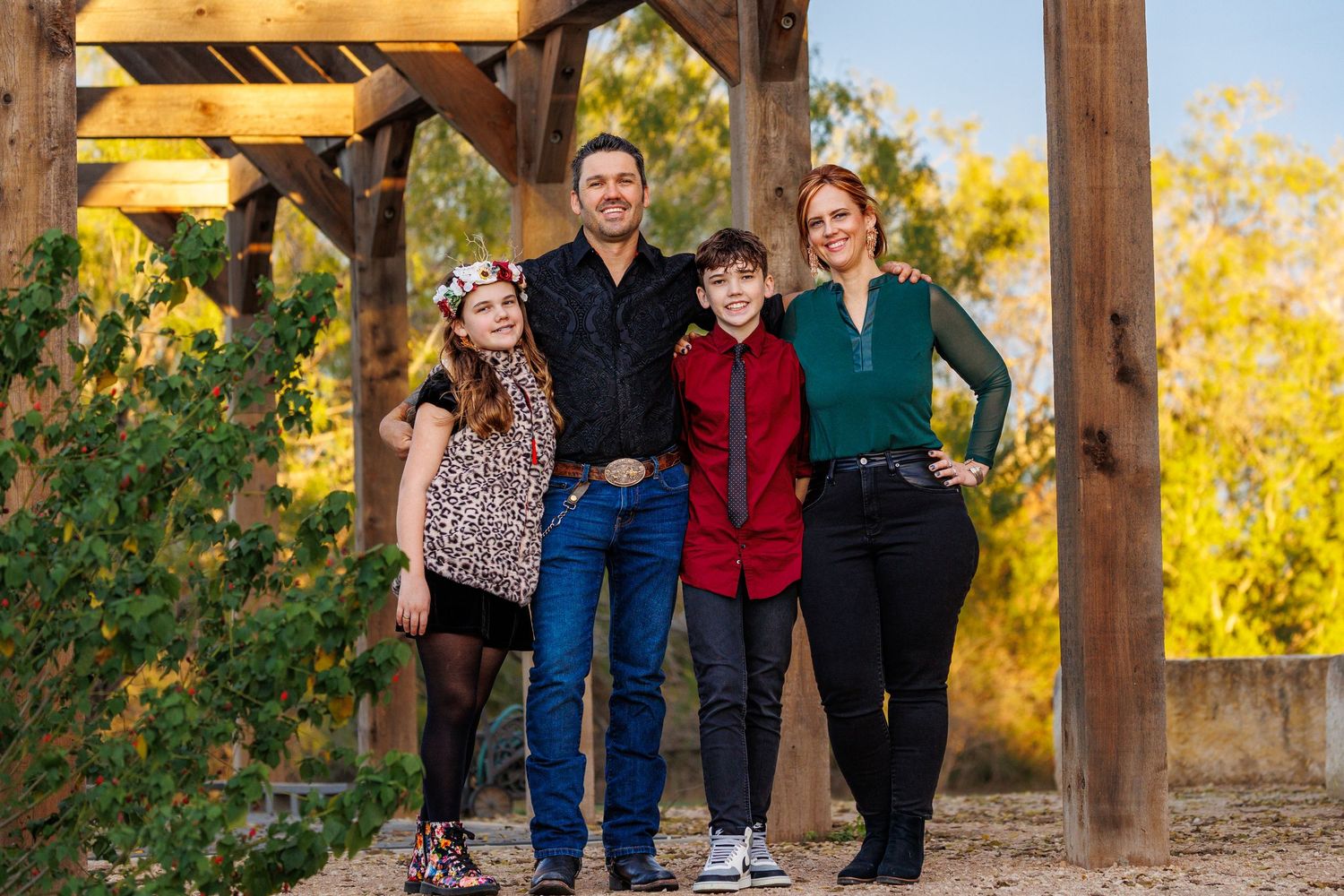 Family of four posing together under wooden pergola during golden hour.