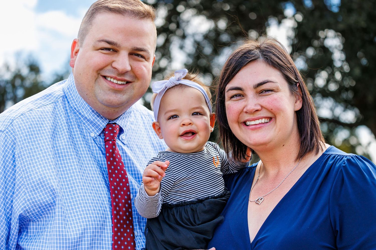 Happy family of three posing together outdoors on a sunny day.