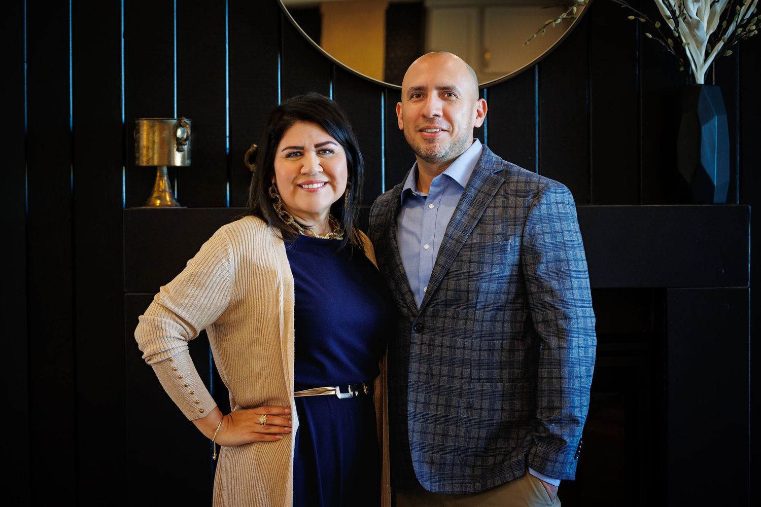 A couple in formal attire poses together in a dark studio setting with professional lighting.
