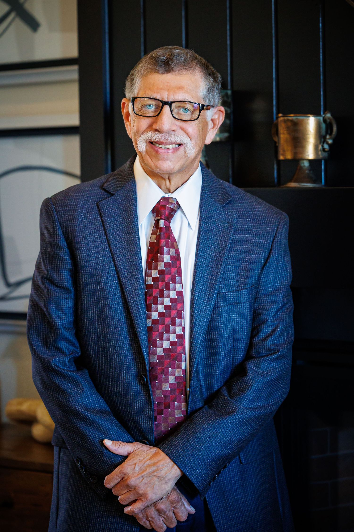 Professional wearing navy suit and red patterned tie smiles warmly in business portrait series.