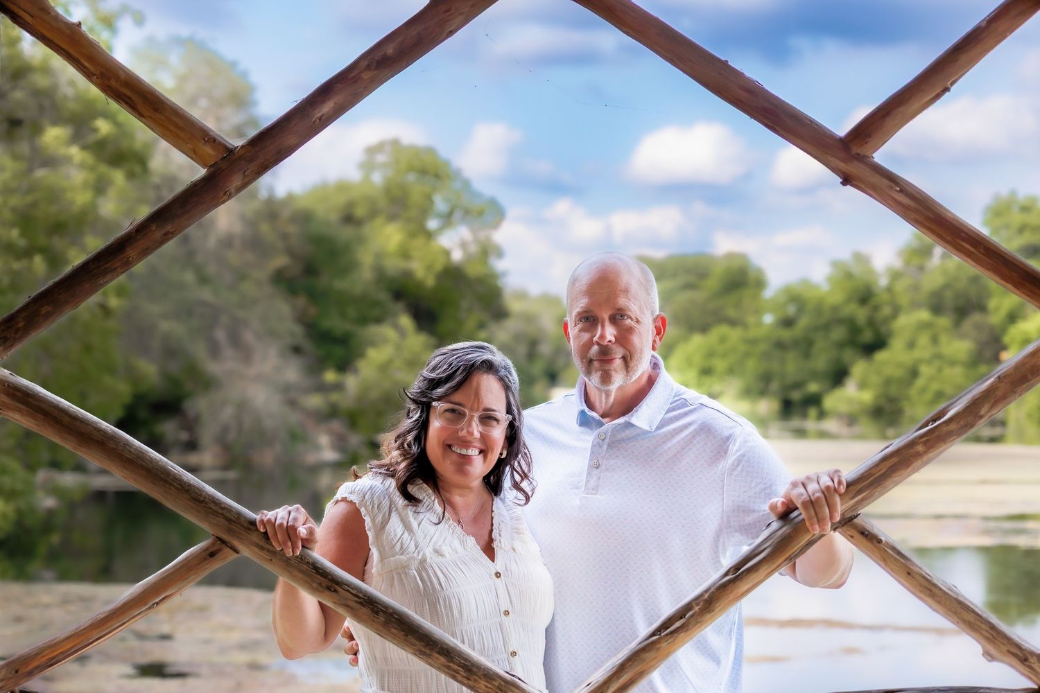 A mature couple smiles while posing together through a rustic metal bridge frame outdoors.