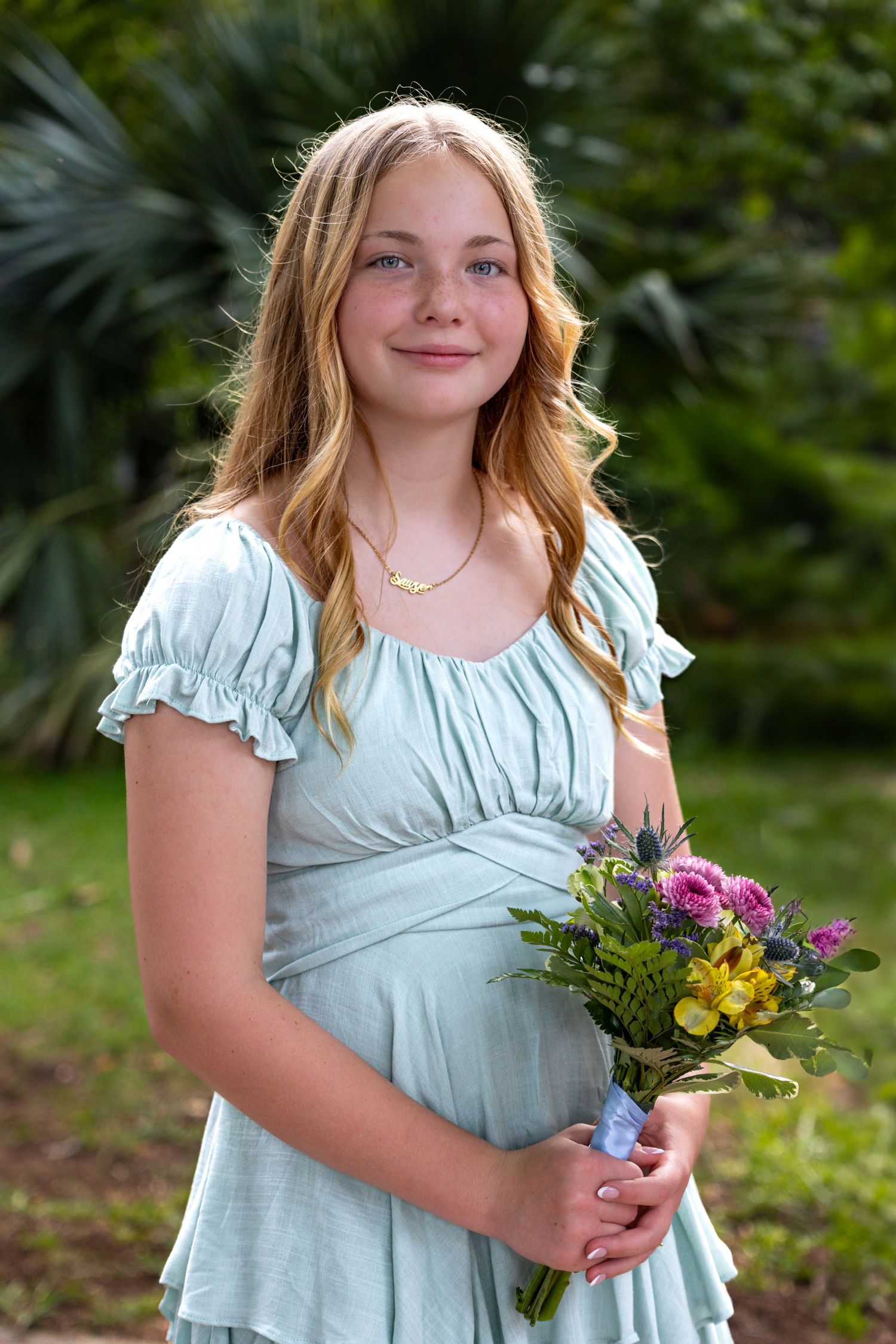 A young person in a light blue dress holding a colorful bouquet outdoors.