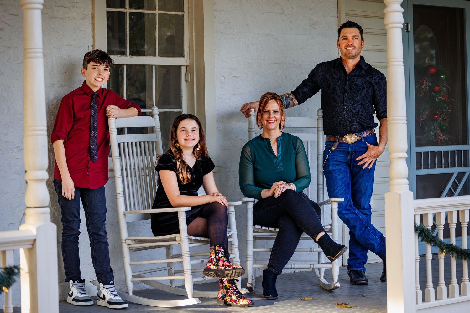 Group portrait of four people relaxing on a white porch with rocking chairs.