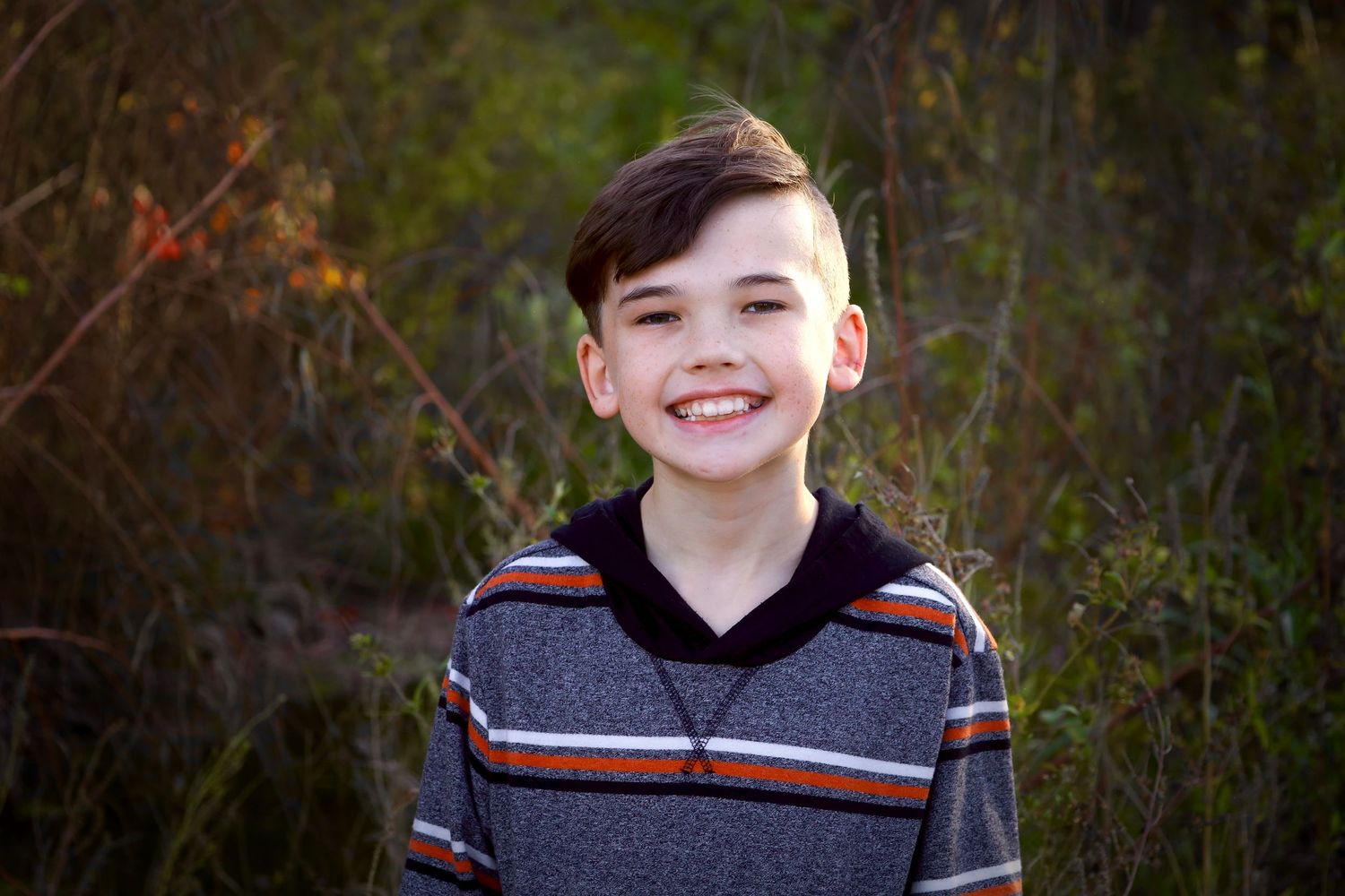 Child in striped sweater smiling outdoors during fall.