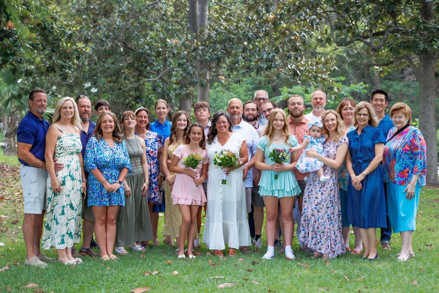 Large group photo of wedding guests and family members gathered outdoors in summer attire.