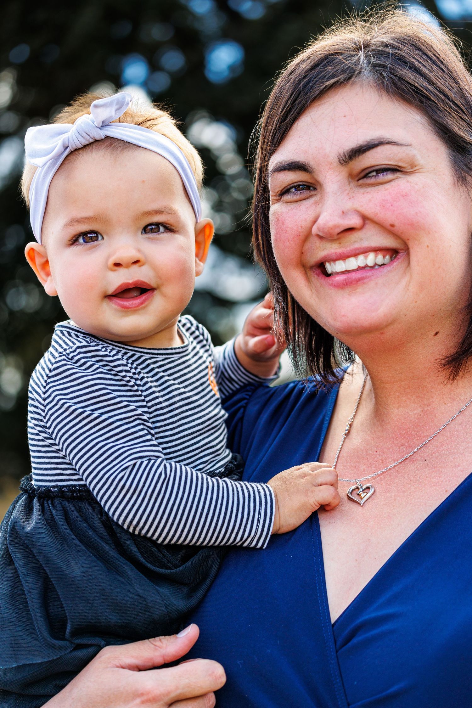 Mother and baby in matching navy outfits smiling at the camera outdoors.
