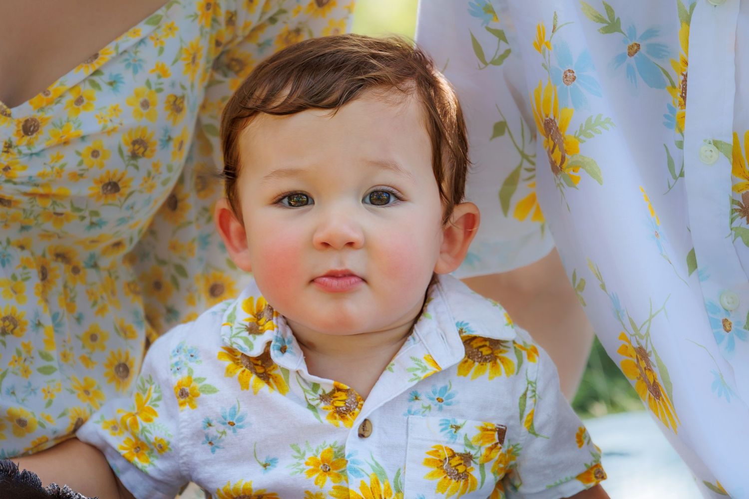 Close up of a toddler wearing a white and yellow floral shirt smiling at the camera.