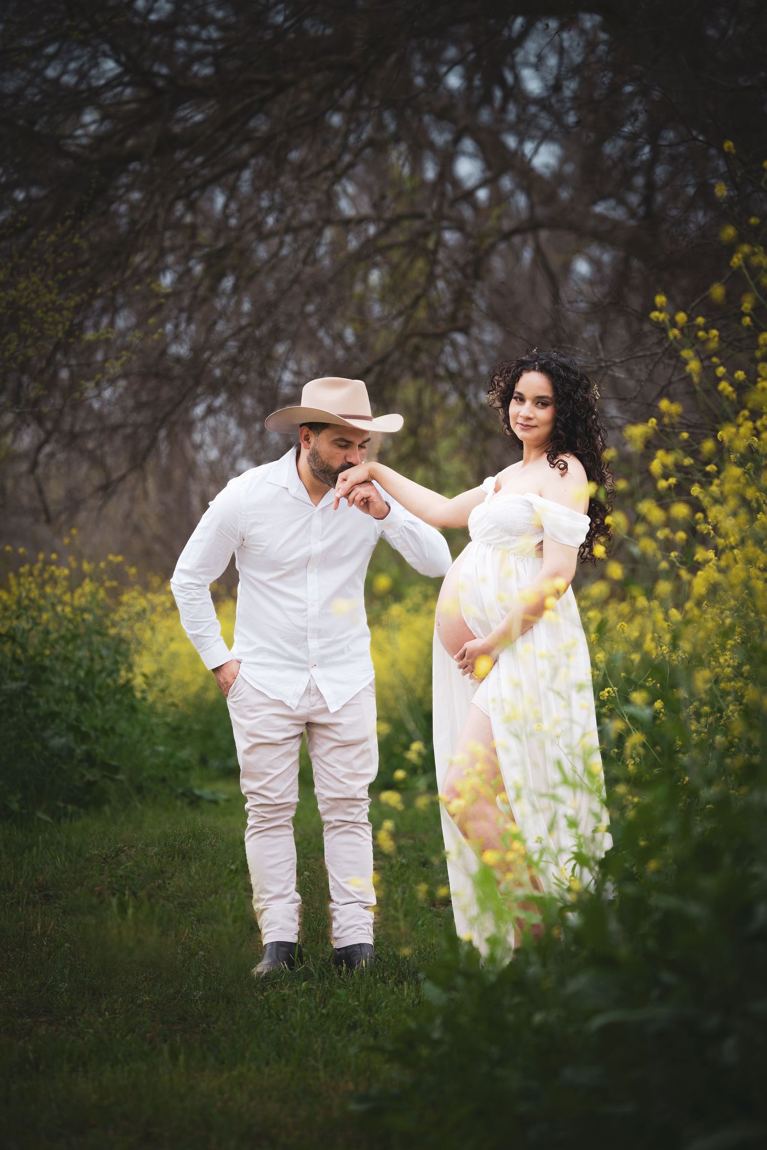 A couple in white attire poses playfully in a field of yellow wildflowers during a spring photoshoot.