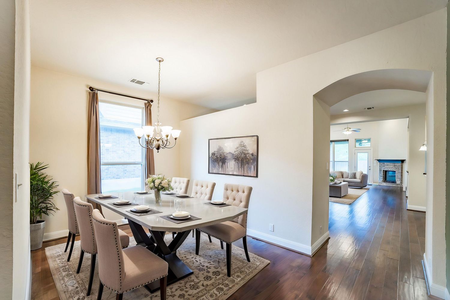 Elegant dining room with crystal chandelier, dark wood floors, and arched entryway leading to kitchen.
