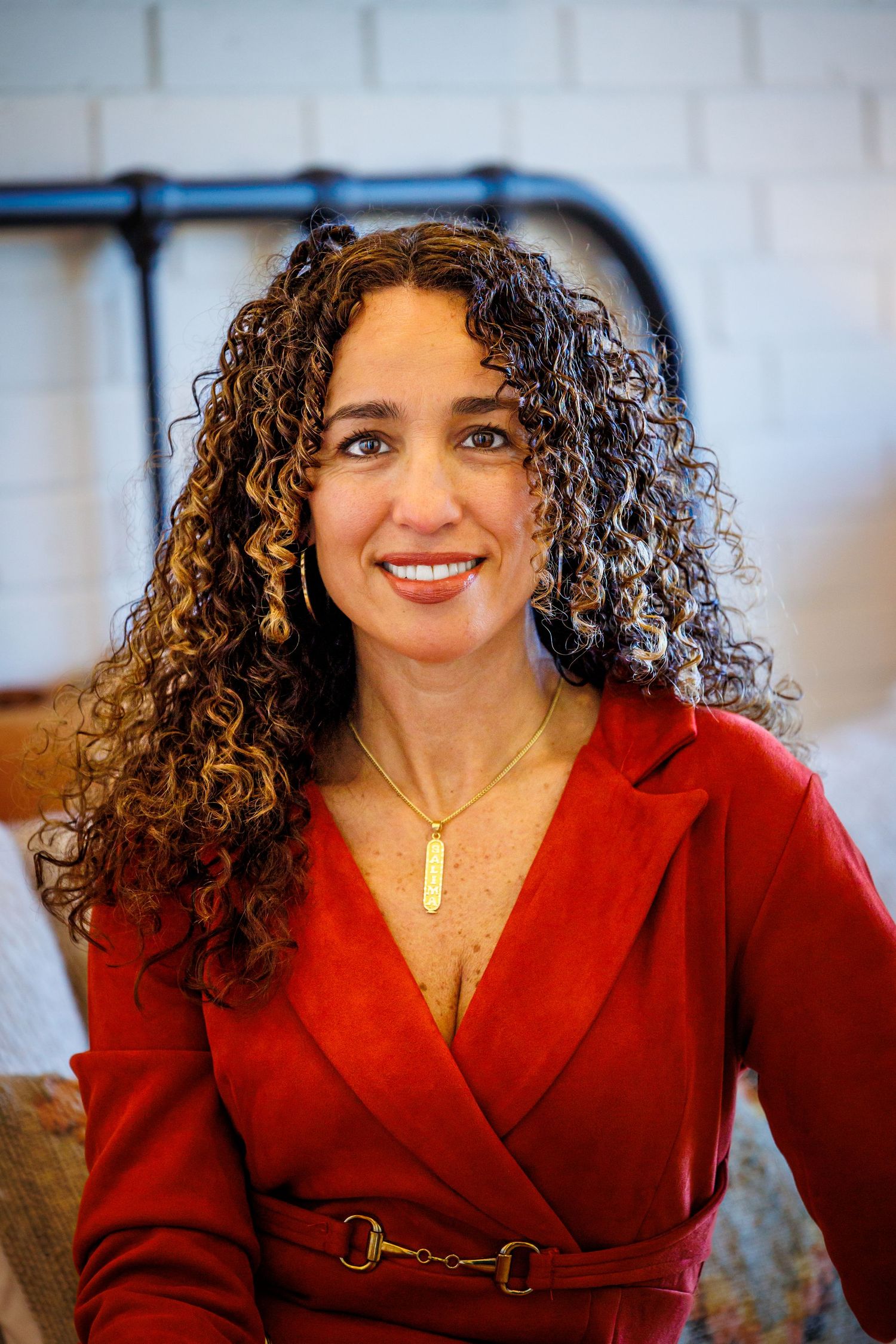 Professional portrait of someone with long curly brown hair wearing a red blazer with a gold necklace.