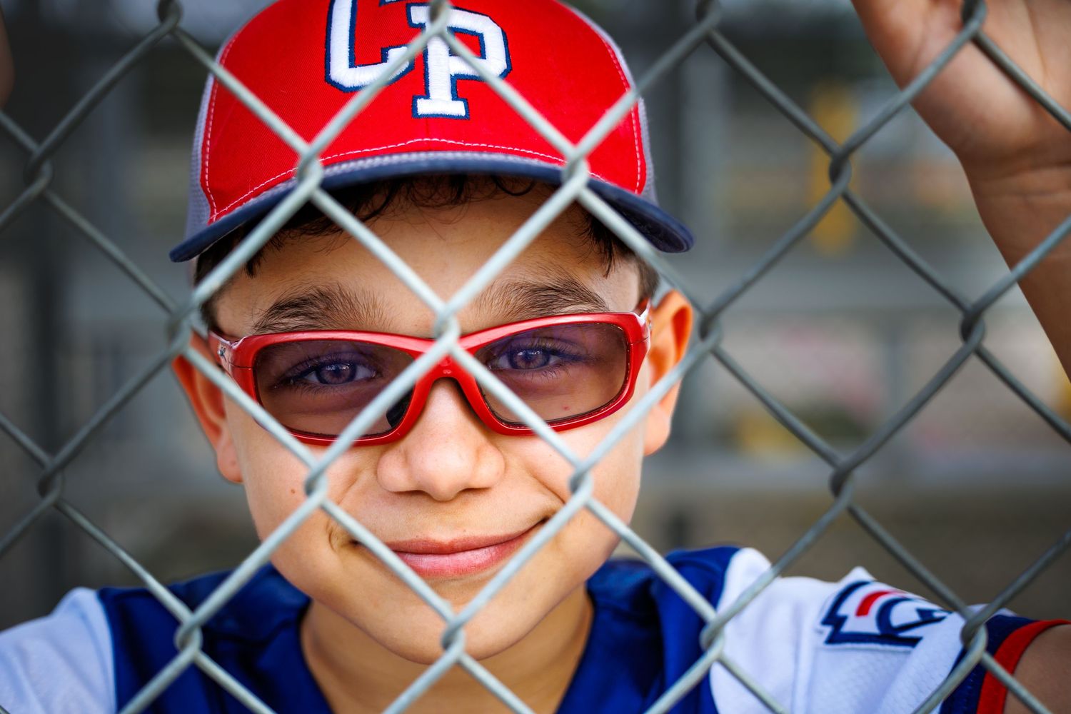 Baseball player in red CP cap and sunglasses seen through chain link fence.