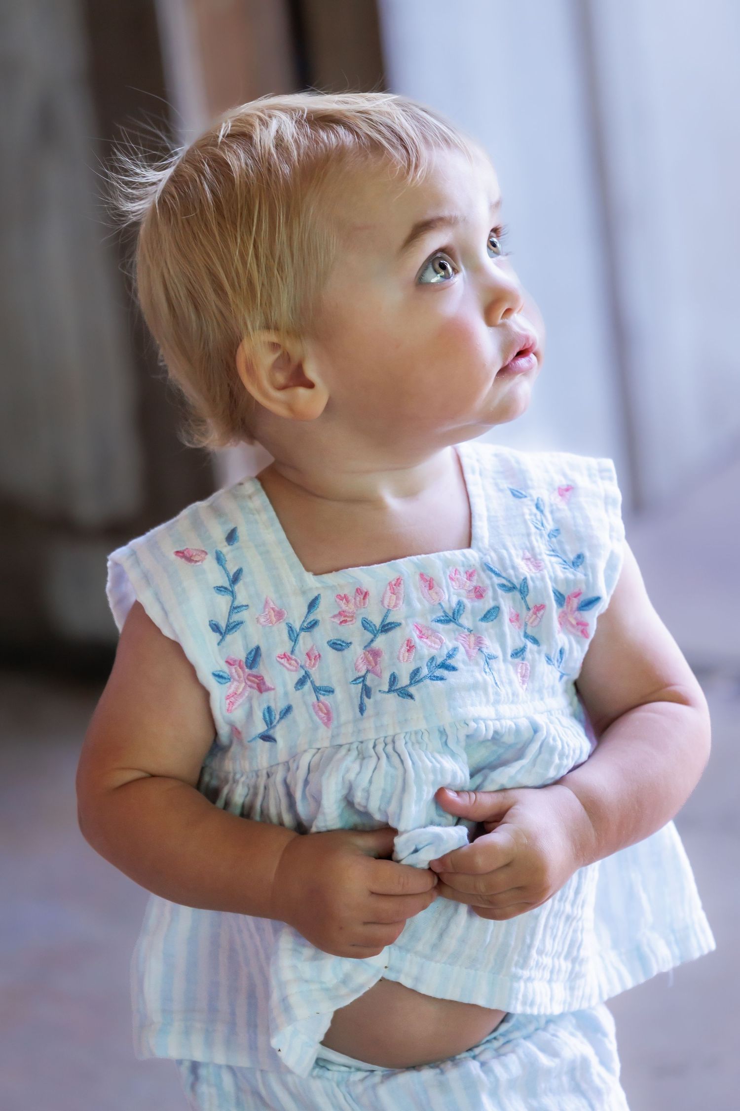 A toddler in a floral print dress looking upward with wonder.