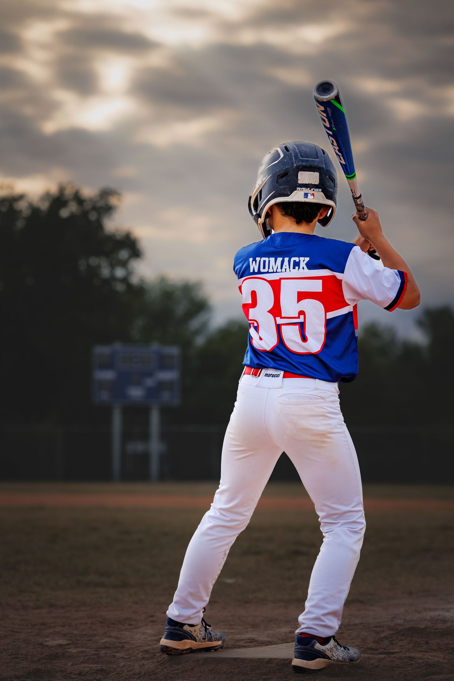 Youth baseball player in batting stance wearing jersey number 35 at sunset.