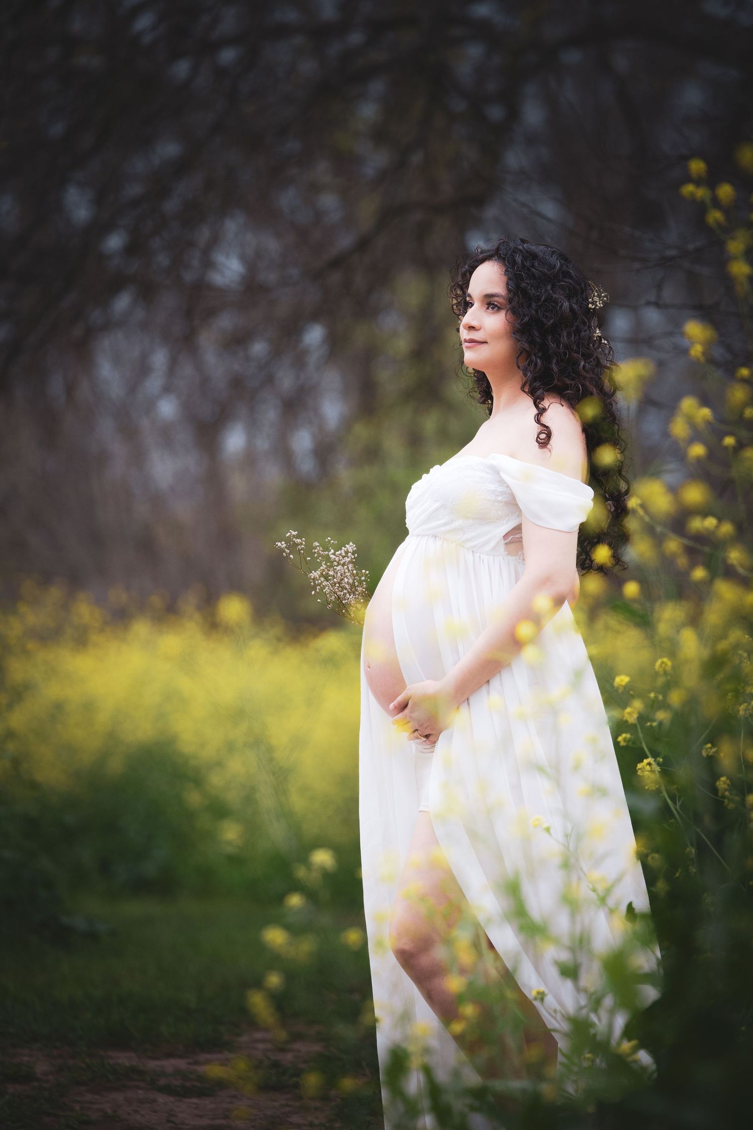 Ethereal maternity portrait in white dress among spring flowers and foliage.