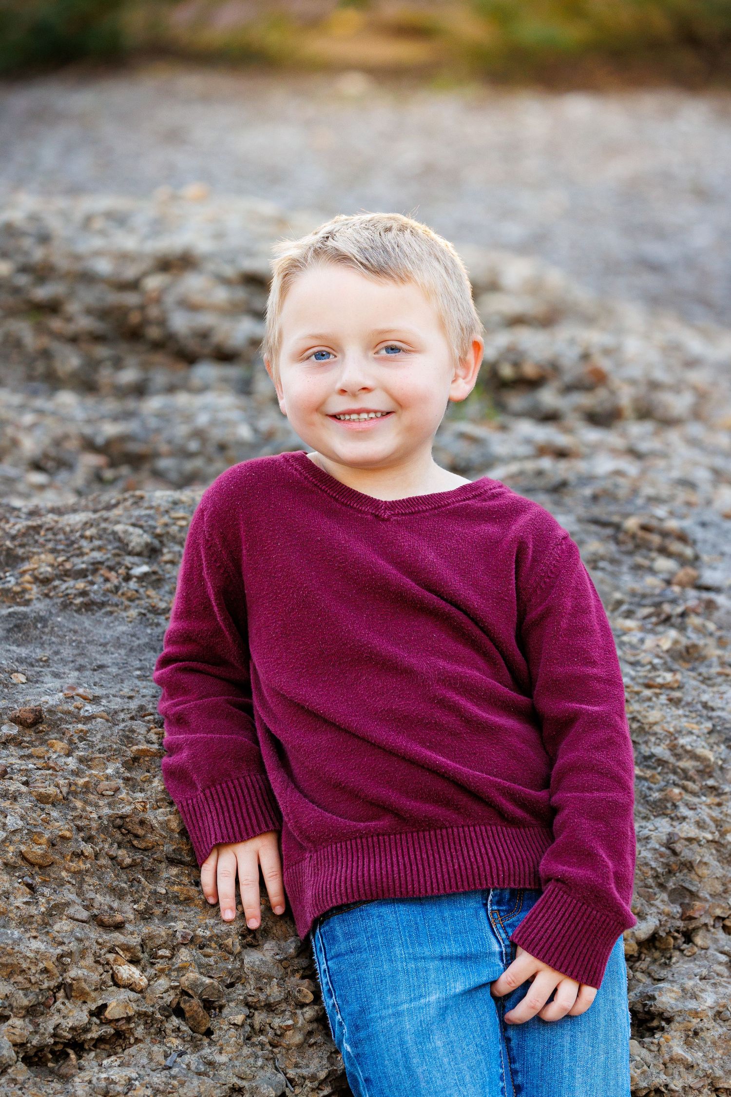 Casual portrait of someone in a burgundy sweater and jeans sitting on rocks.