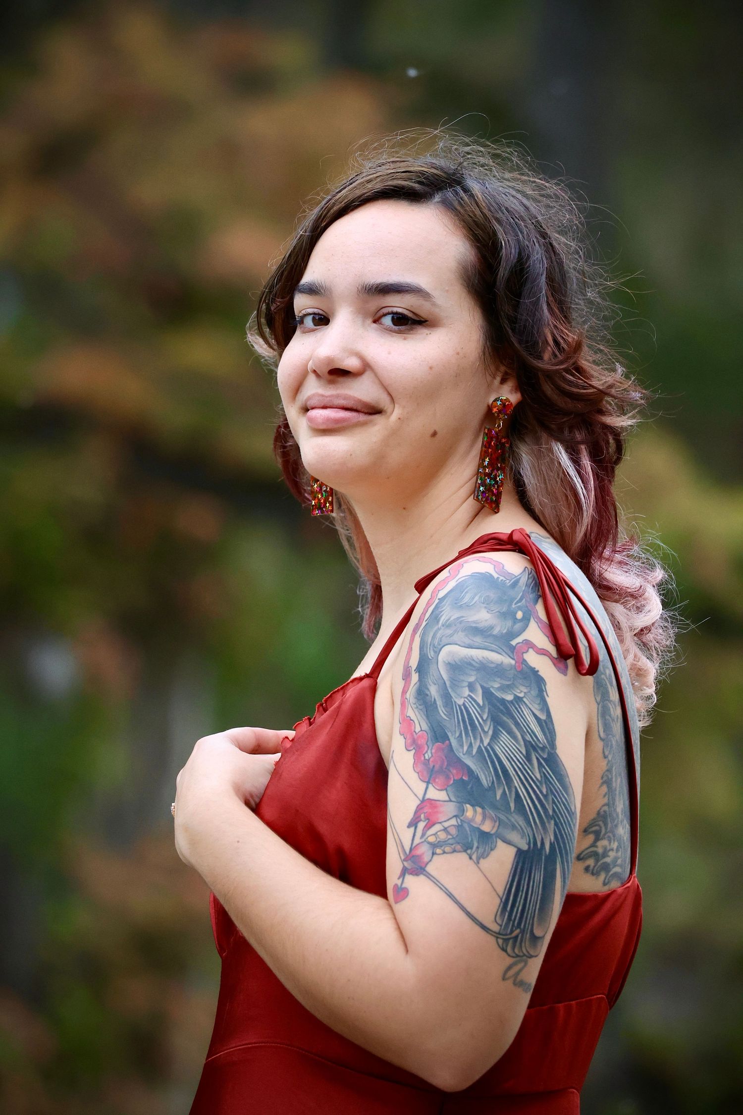 Woman in red dress with visible arm tattoos poses outdoors.