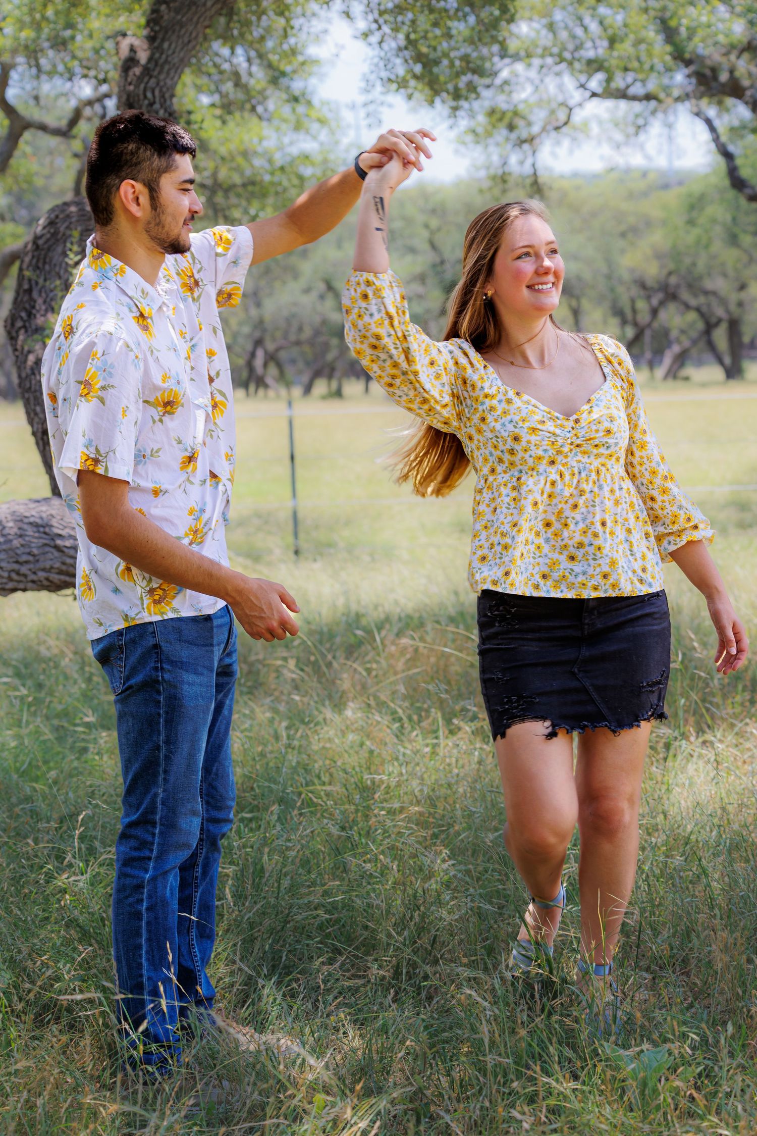 Couple in matching yellow floral outfits dancing and laughing in outdoor field.