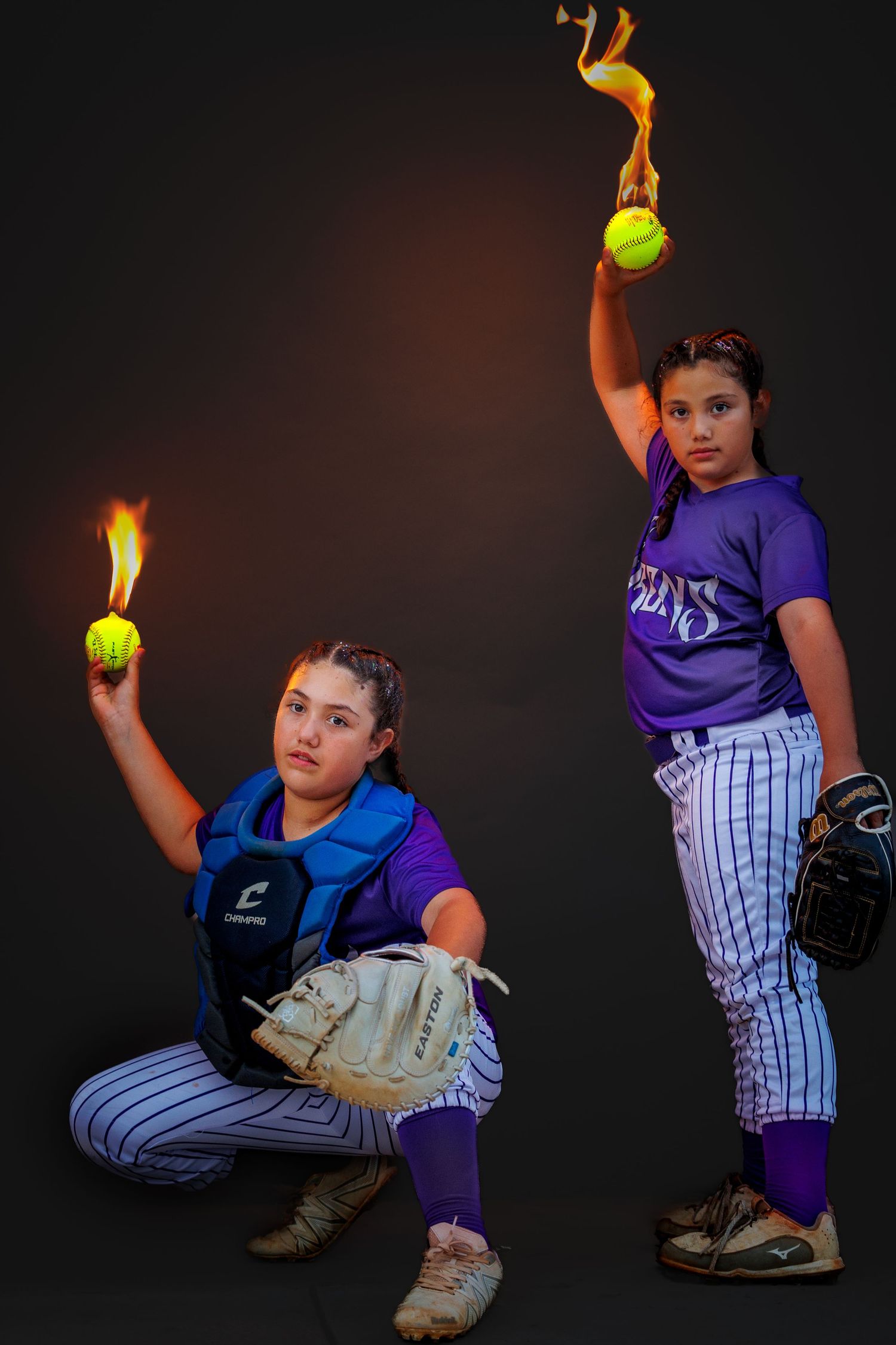 Two softball players in striped pants pose with flaming tennis balls in dramatic dark studio photo.