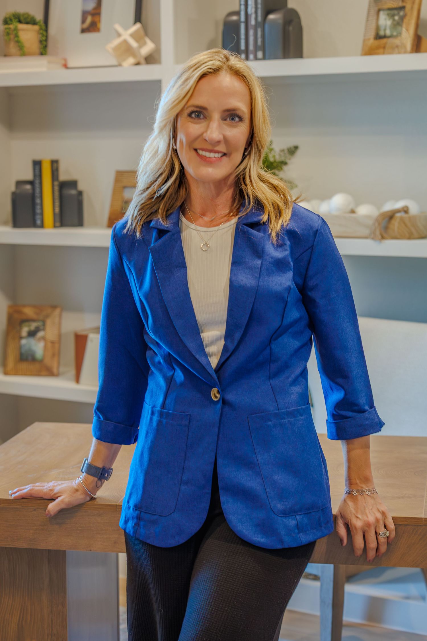 Professional wearing a bright royal blue blazer stands in front of white built-in shelving in an office setting.