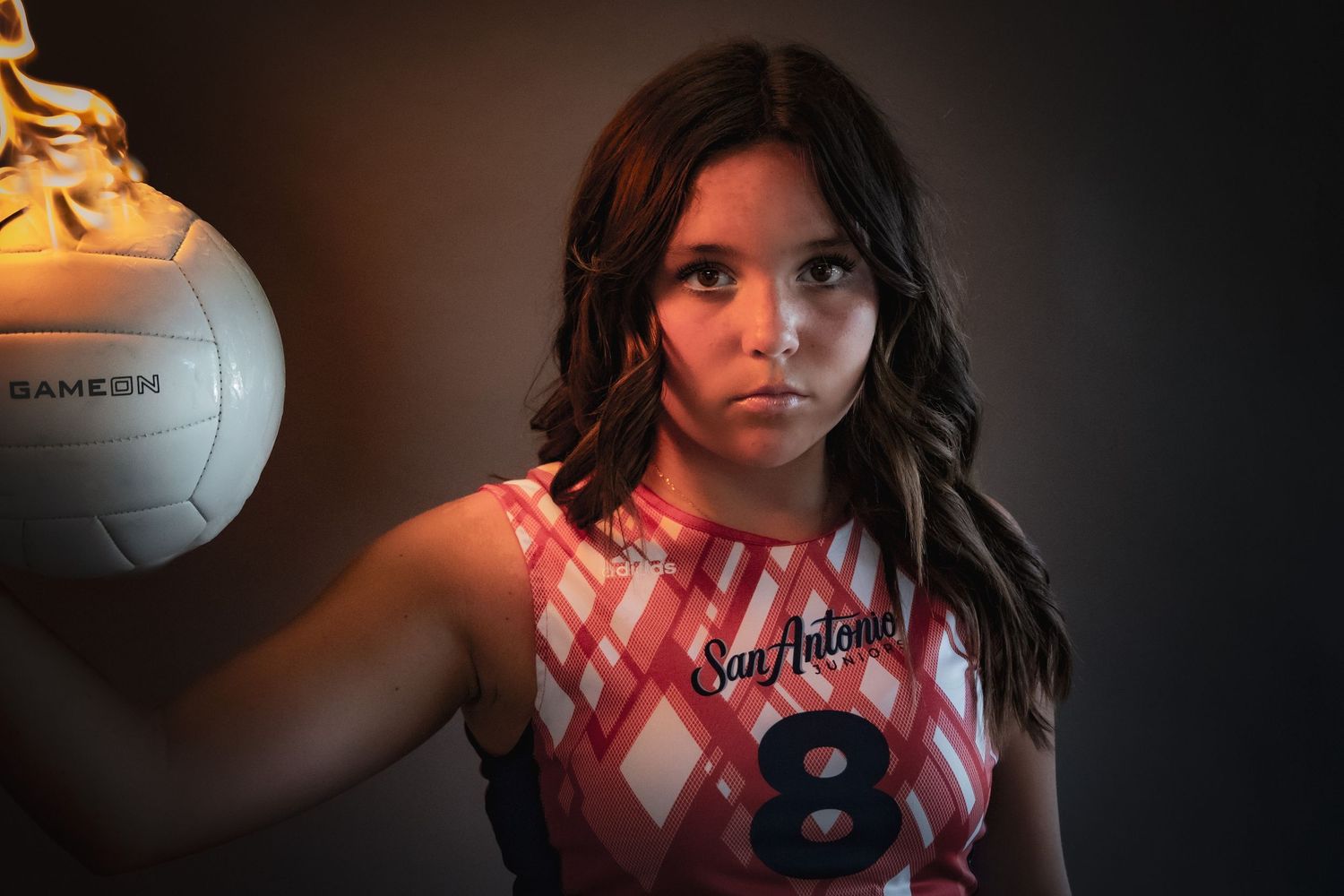 A volleyball athlete in red and white uniform poses confidently against a dramatic background lighting setup.