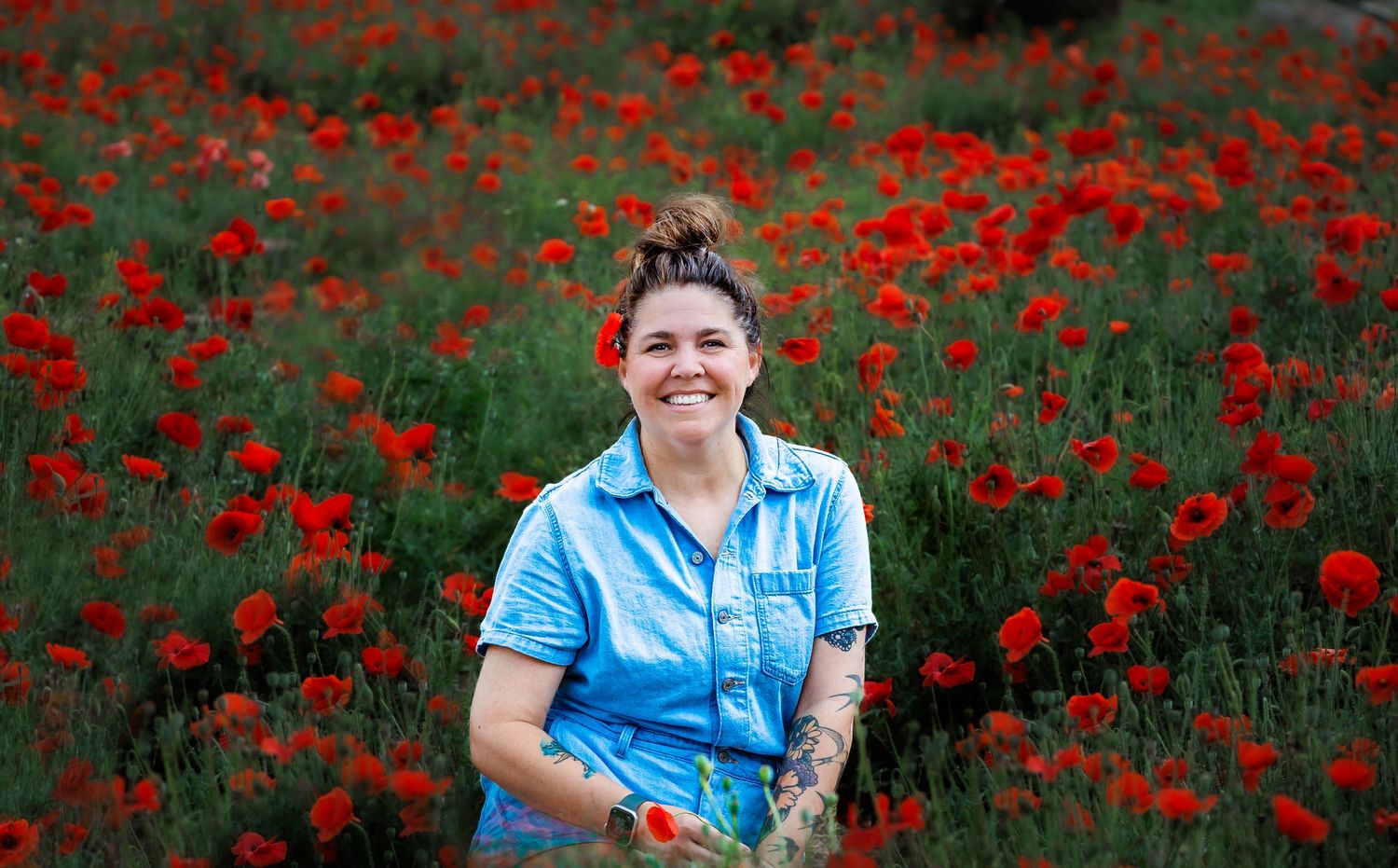 A beautiful field of vibrant red poppies with a person in a blue shirt smiling among the flowers.