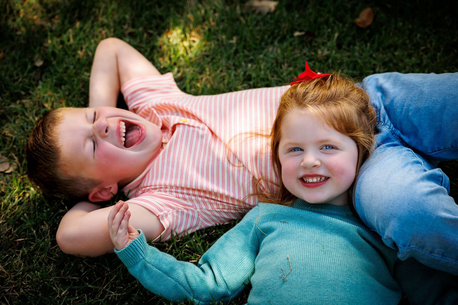 Two people lying on grass and laughing together on a sunny day.