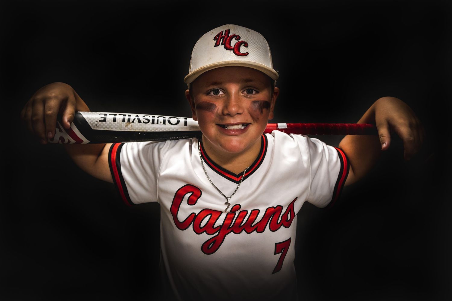 Baseball player in white Cajuns uniform poses with bat across shoulders against dark background.