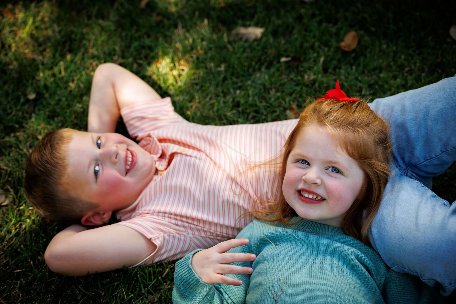 Two joyful children laying on green grass outdoors during a sunny day.