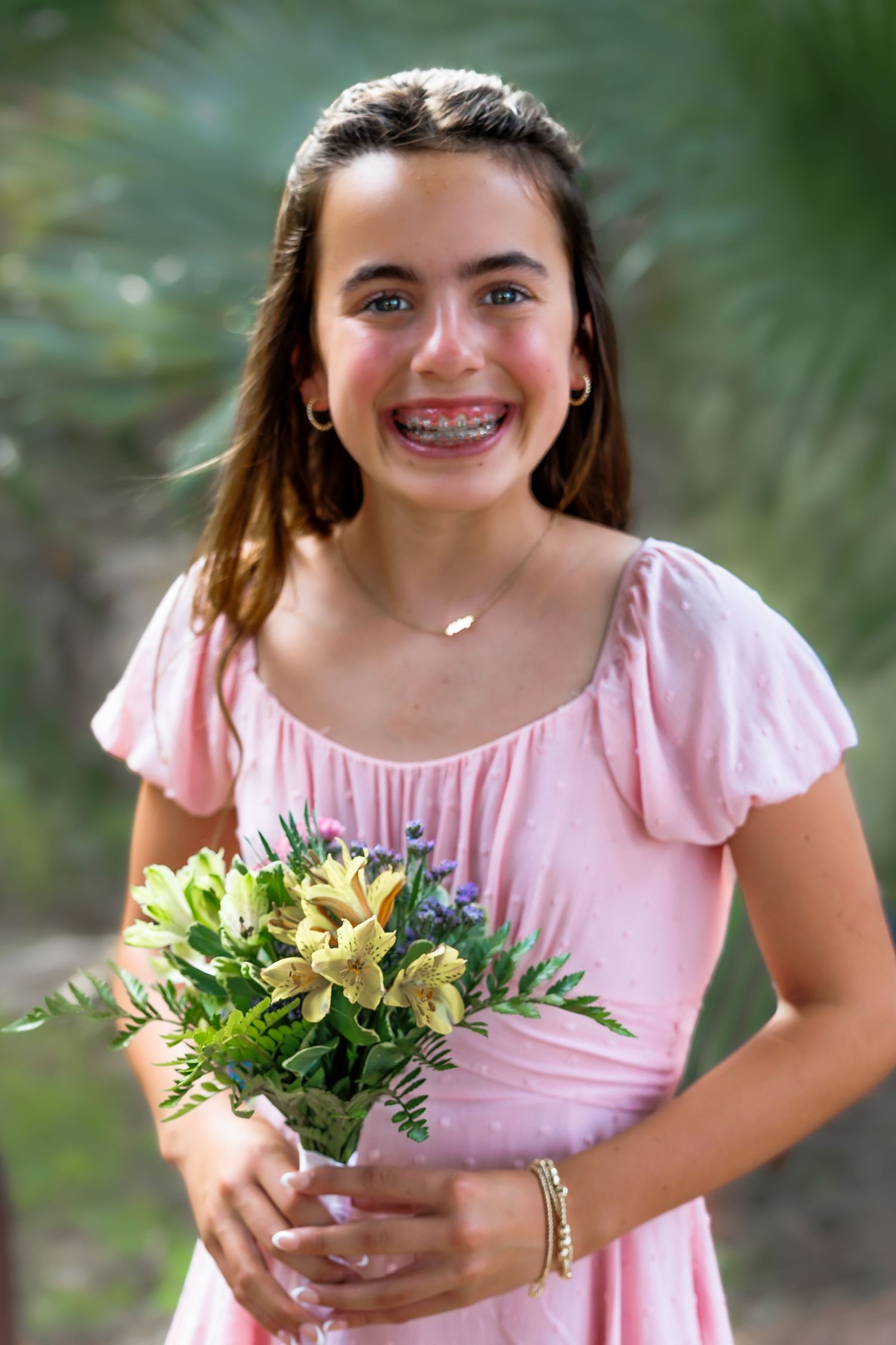Young person in pink dress holding yellow wildflower bouquet outdoors in summer garden setting.