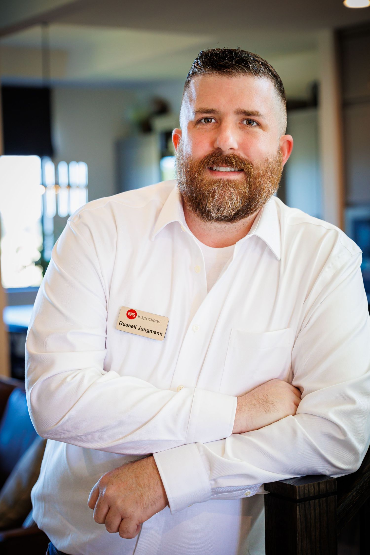 Chef in white uniform with beard stands confidently with crossed arms in restaurant kitchen.