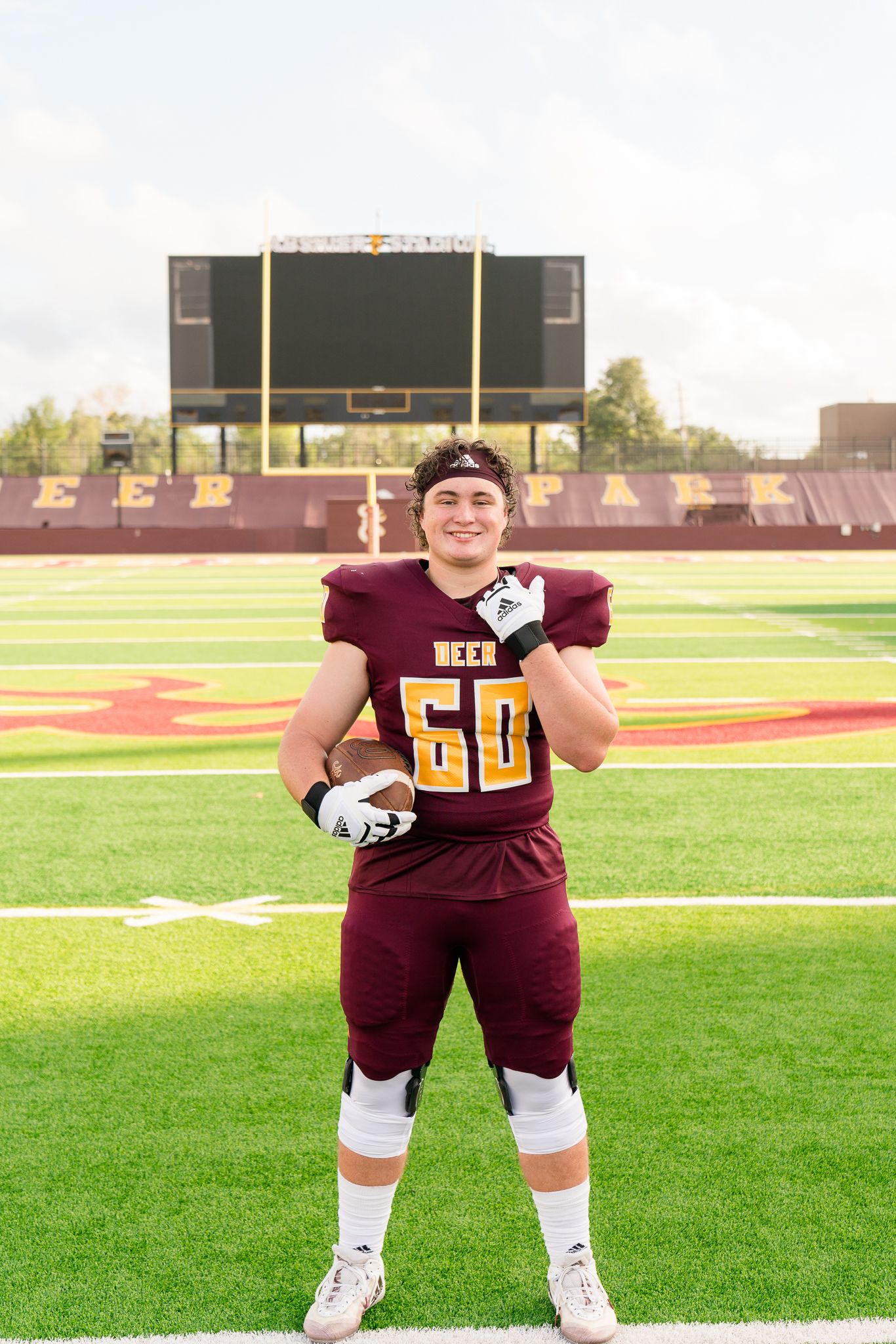 Football player wearing maroon #60 jersey poses on field at Deer Park stadium.