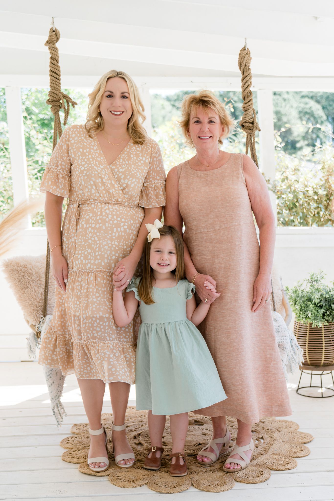 Three generations of women, grandmother, mother, and young daughter, pose together in a bright white studio.