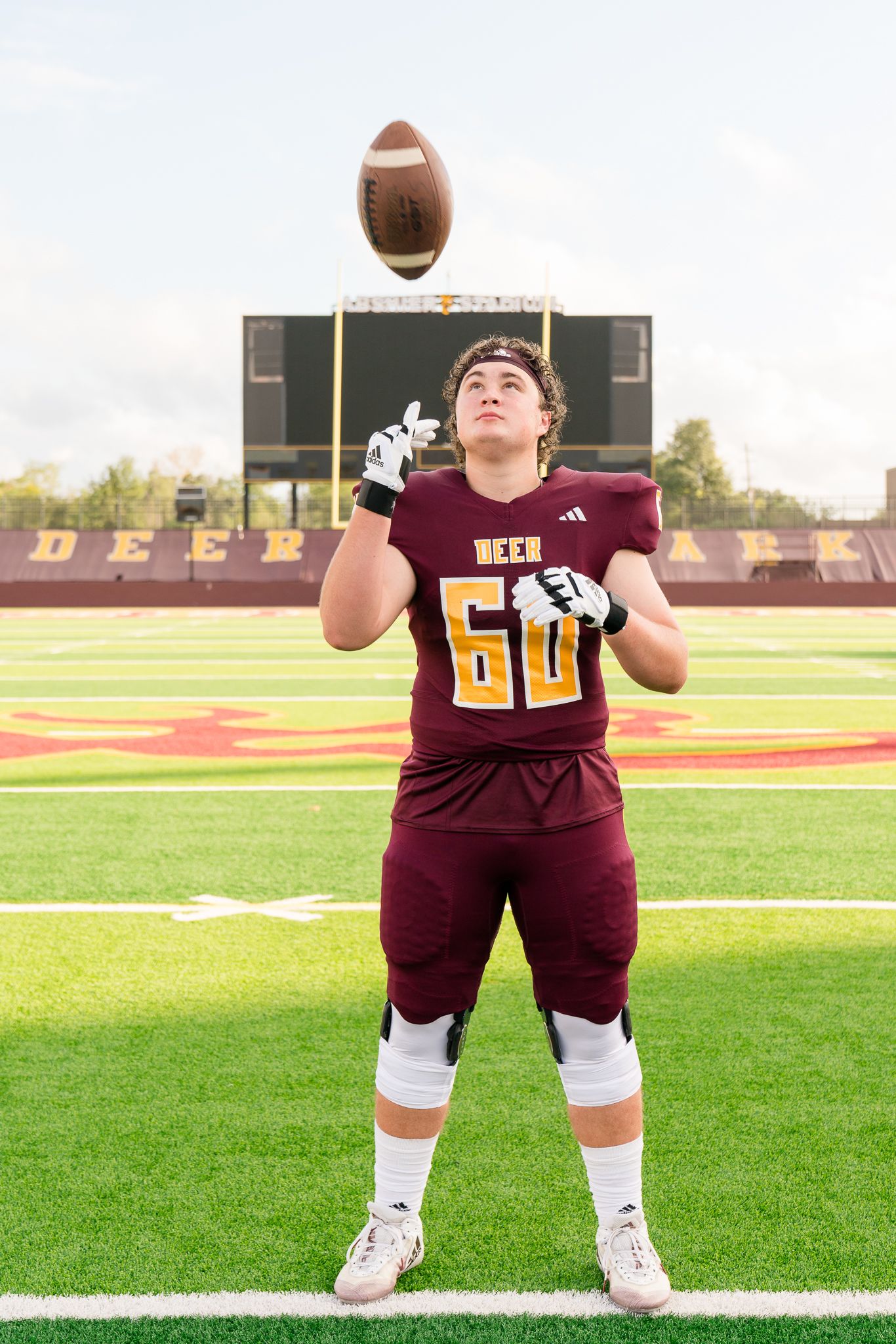 High school football player #60 in maroon uniform tossing a football at Deer Park stadium.
