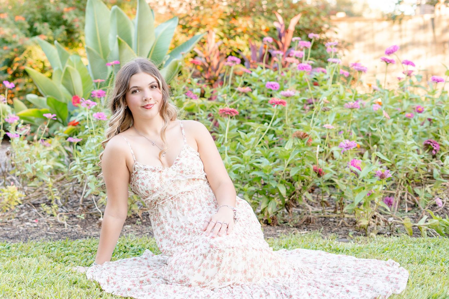 Young woman in floral maxi dress sitting gracefully in a colorful garden with blooming flowers.