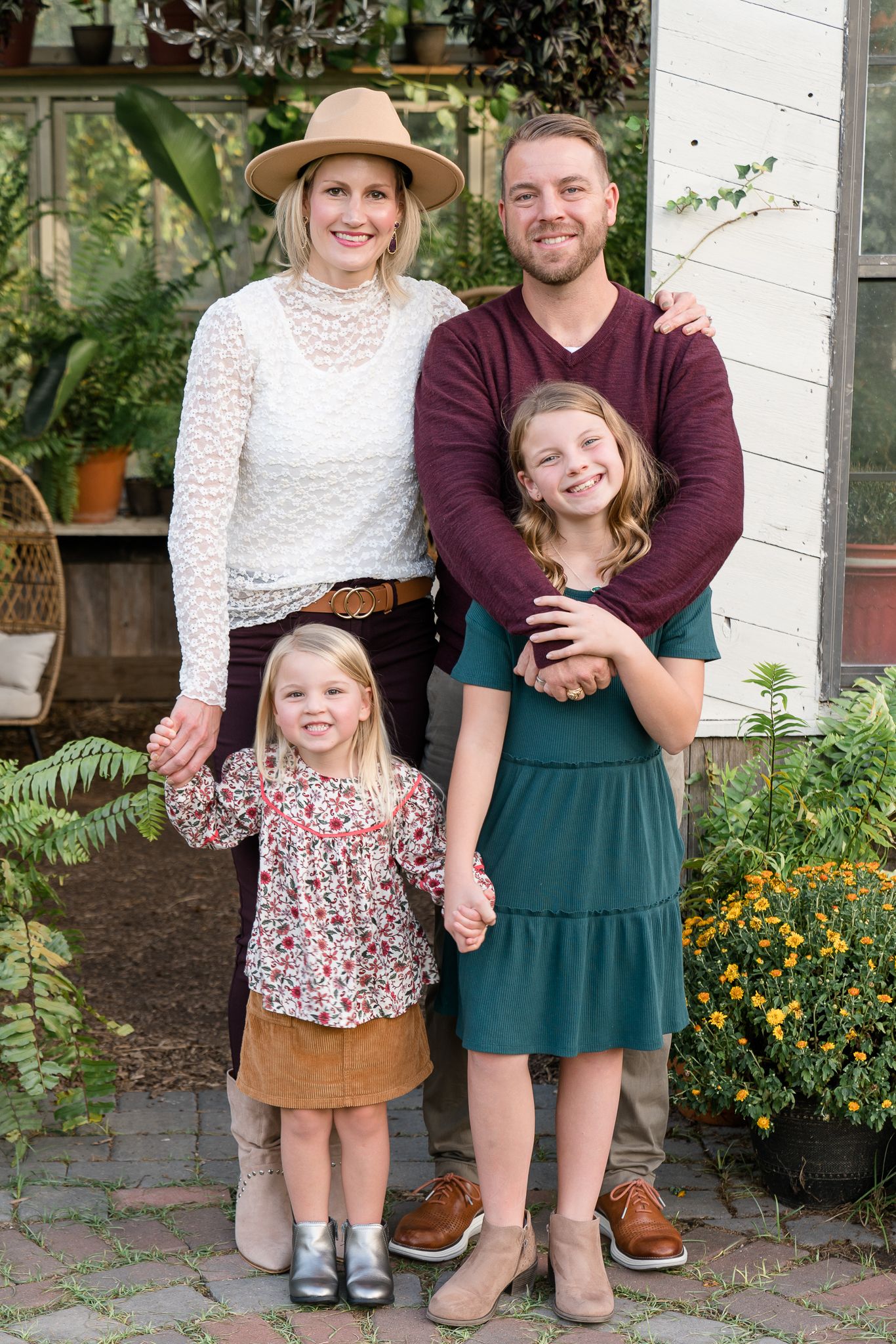 A happy family of four poses outdoors in fall attire, with two daughters and parents smiling together.